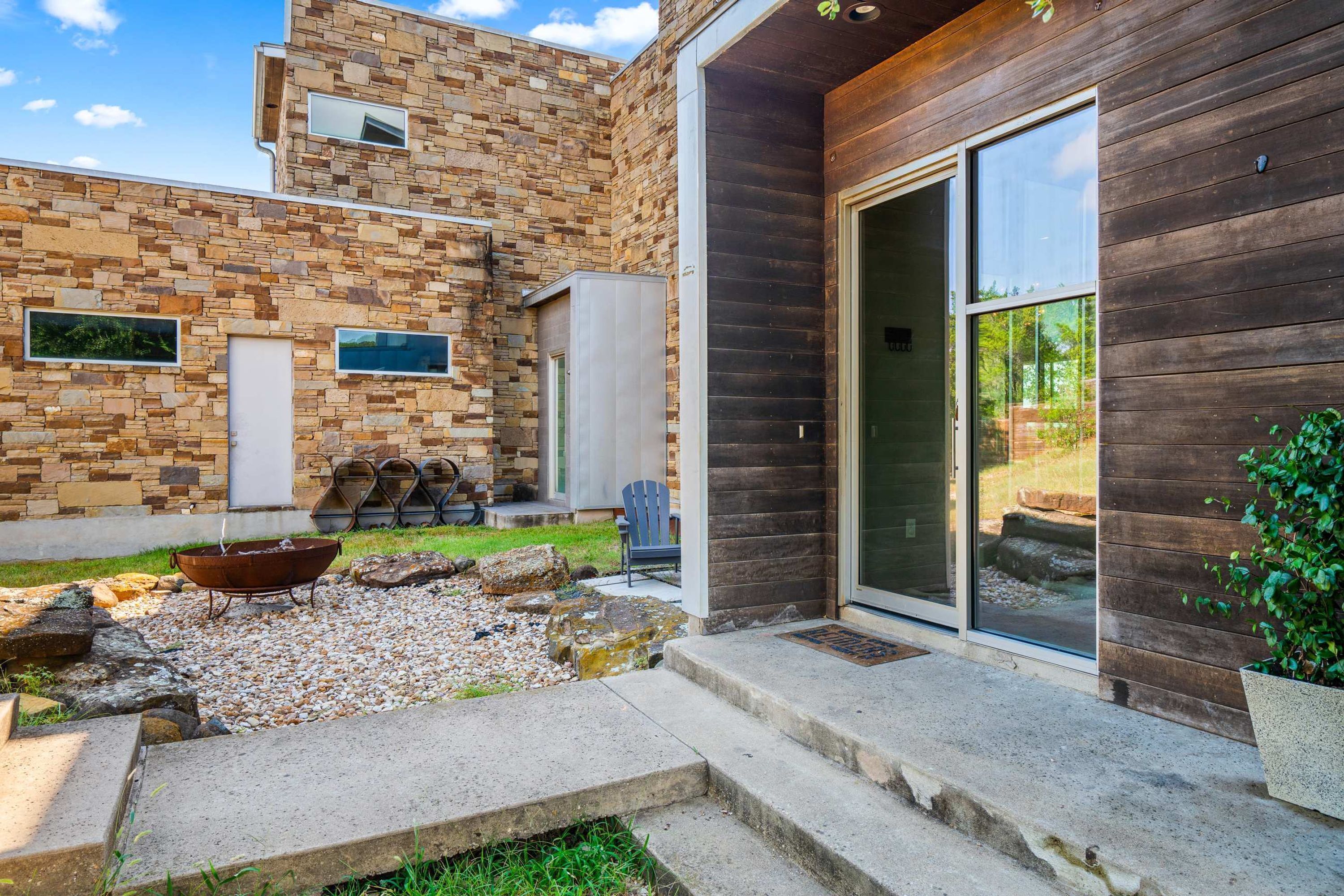 Une maison moderne avec une façade en pierre, une terrasse en bois et une grande porte-fenêtre coulissante.