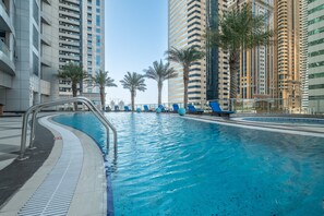 A swimming pool with blue water, surrounded by tall buildings and palm trees. - Stayshort - Modern 1 Bedroom Getaway Sleeps 4 in Dubai Marina (Dubai)