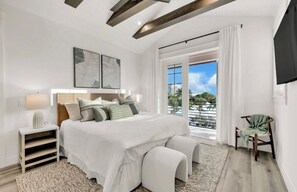 A bedroom with a large bed, a nightstand, a chair, and a view of the outdoors. - New! Beach House with heated pool/spa water slide! (Siesta Key)