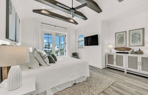 A modern bedroom with a large bed, a ceiling fan, a TV, and a view of the city. - New! Beach House with heated pool/spa water slide! (Siesta Key)