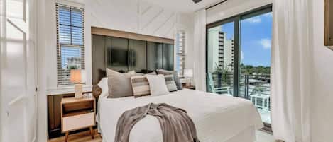 A modern bedroom with a large bed, a ceiling fan, and a view of a cityscape through a large window.