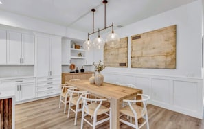 Eine moderne Küche mit weißen Schränken, einem Holztisch und Pendelleuchten.