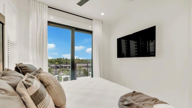 Un dormitorio con una cama grande, un televisor de pantalla plana montado en la pared y un balcón con vistas a zonas verdes.