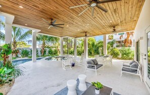 An outdoor covered patio with seating, a pool, and a view of the surrounding greenery. - New! Beach House with heated pool/spa water slide! (Siesta Key)