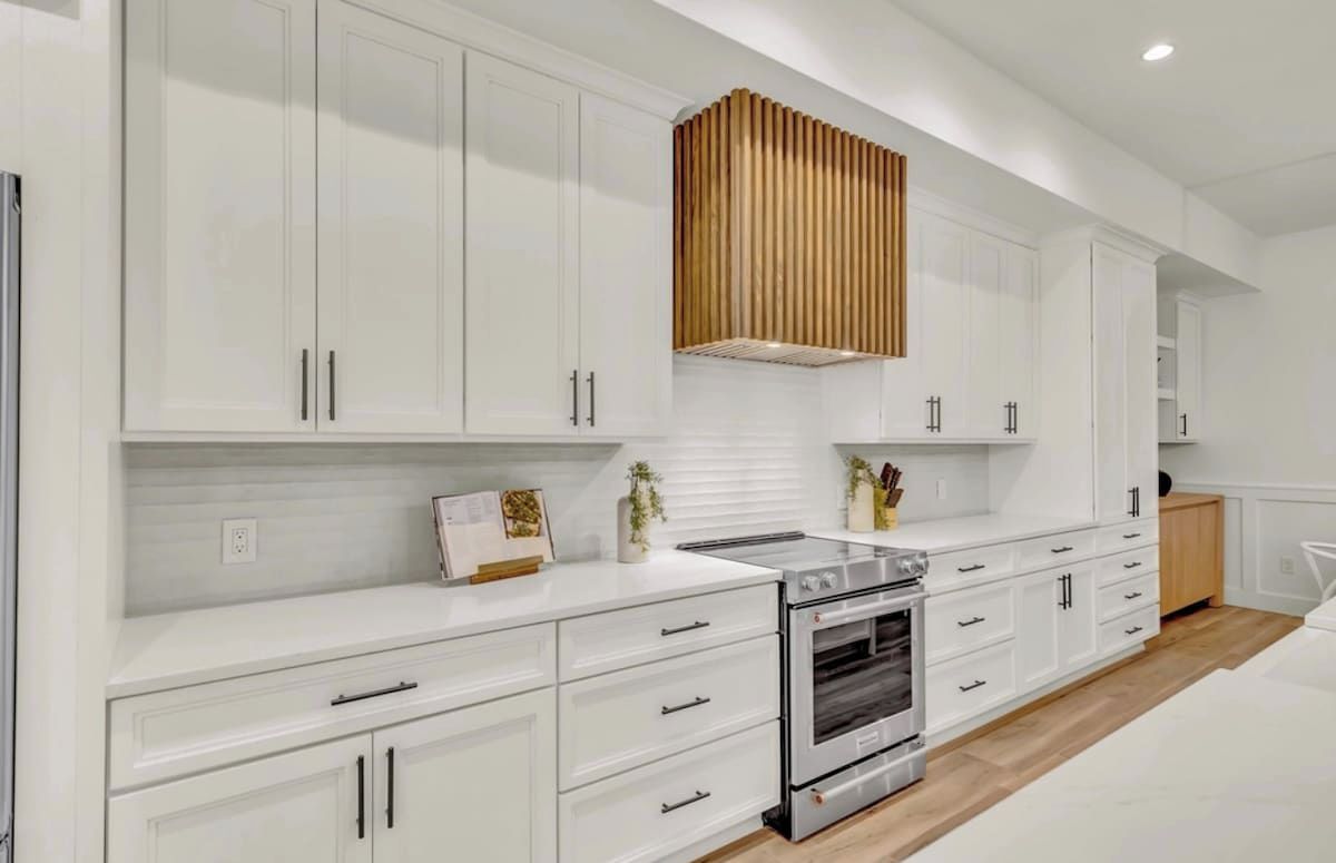 A modern kitchen with white cabinetry, a built-in oven, and a wooden accent wall.