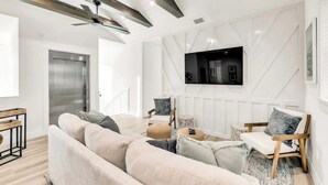 Una sala de estar moderna con un sofá, sillas, un televisor montado en la pared y un ventilador de techo.