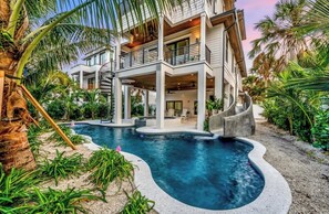 Ein modernes, mehrgeschossiges Haus mit Swimmingpool, umgeben von tropischer Vegetation.