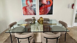 Un espace repas moderne avec une table à plateau en verre, quatre chaises rembourrées et deux grandes peintures représentant des flamants roses, accrochées au mur.