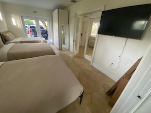 Ein Hotelzimmer mit drei Betten, einem an der Wand montierten Fernseher und einer Tür zu einem Parkplatz.