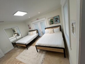 Ein Schlafzimmer mit zwei Einzelbetten, einem großen Spiegel, einer Tür mit Ausgangsschild und zwei gerahmten Bildern von tropischen Blättern.