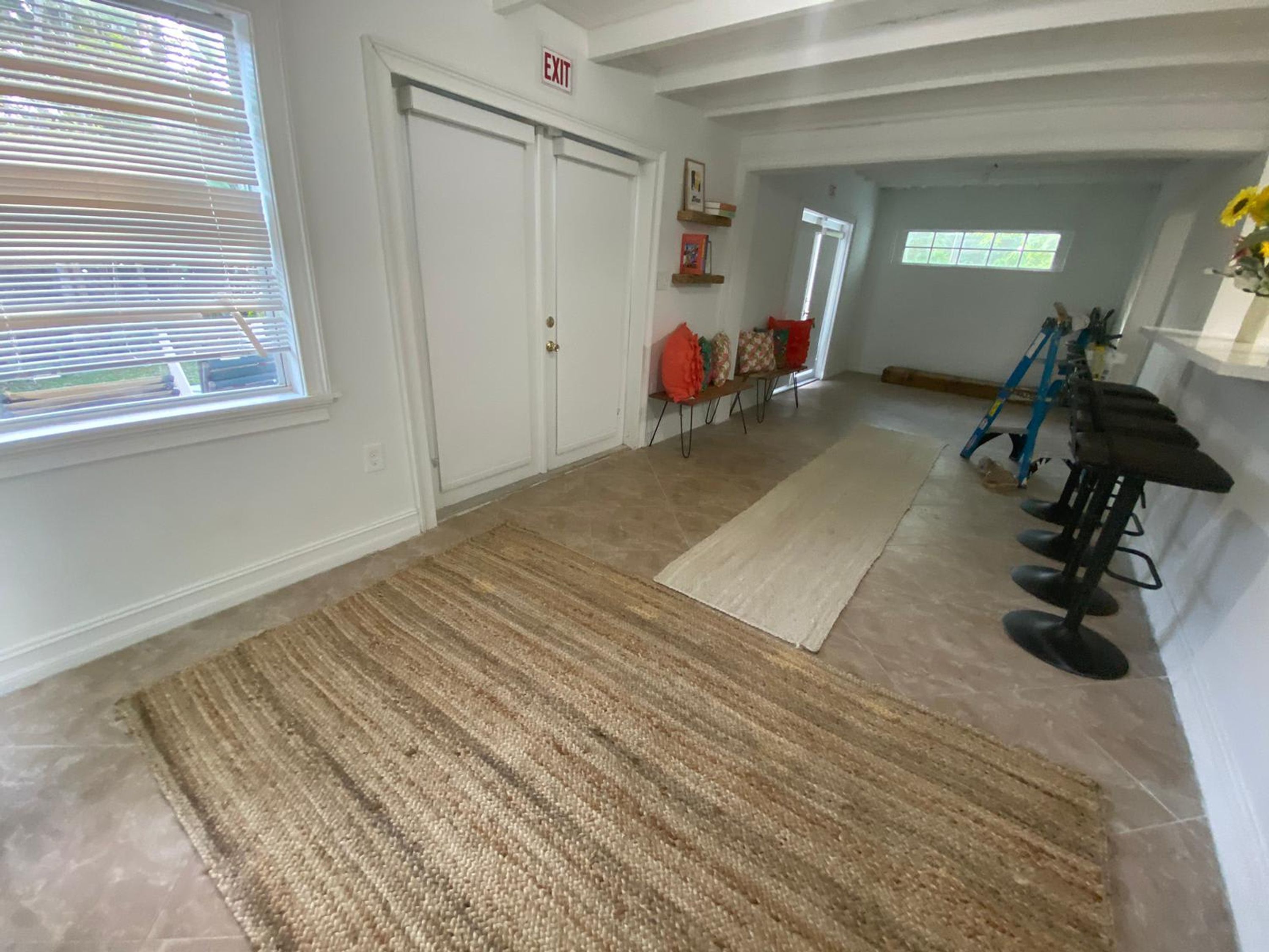 A hallway with a rug, a door marked "EXIT", a window with blinds, and a chair with a red cushion.