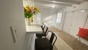 Un espace repas moderne avec une table blanche et des chaises noires, un vase rempli de tournesols et un panneau de signalisation indiquant la sortie sur le mur.