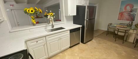 A modern kitchen with white cabinets, a stainless steel refrigerator, and a glass dining table with chairs.
