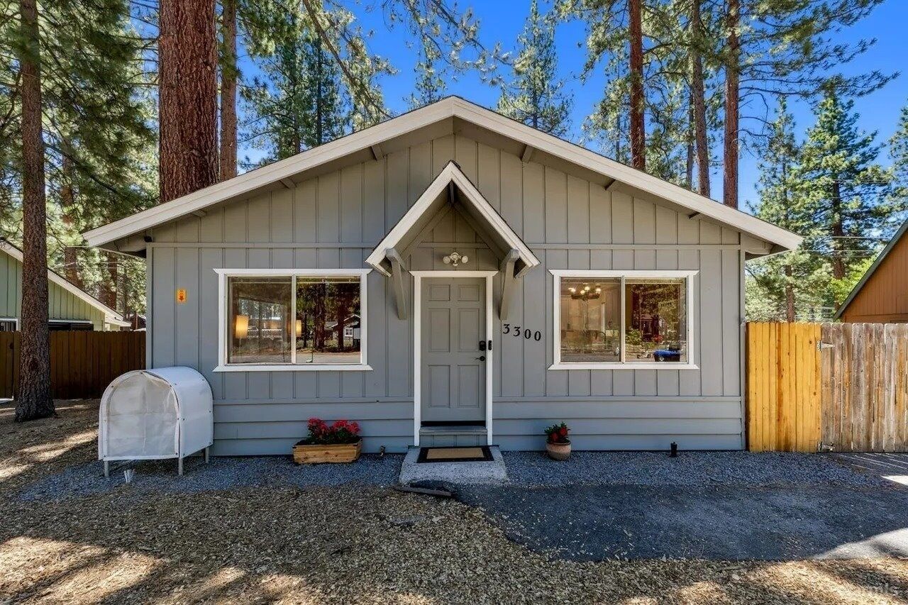 A small, single-story cabin with a gray exterior, a white front door, and two windows on the front facade.