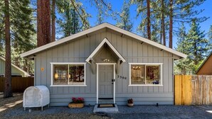 A small, single-story cabin with a gray exterior, a white front door, and two windows on the front facade. - 3300 Cape Horn 3 Bedroom Home (South Lake Tahoe)