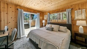 A cozy bedroom with a wooden ceiling, a large bed with a white comforter, two bedside lamps, and a view of the outdoors through a sliding glass door. - 3300 Cape Horn 3 Bedroom Home (South Lake Tahoe)