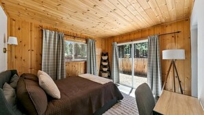 A cozy room with a bed, a desk, and a window overlooking a wooden deck. - 3300 Cape Horn 3 Bedroom Home (South Lake Tahoe)