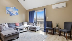 A living room with a gray sofa, a white coffee table, a gray ottoman, a gray armchair, a small table with a plant, and a window with blue curtains. - Pocono Paradise Ultimate Camelback Getaway 4 Bedroom Townhouse (Tannersville)