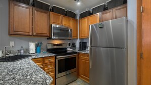 Eine Küche mit Holzschränken, einem Edelstahl-Kühlschrank, einer Mikrowelle, einem Backofen und Granit-Arbeitsplatten.