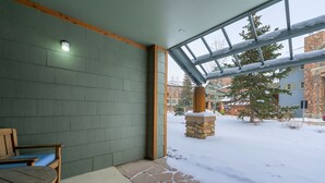 Ein überdachter Patio-Bereich mit Kamin aus Stein, hölzernen Bänken und Blick auf eine verschneite Nachbarschaft.