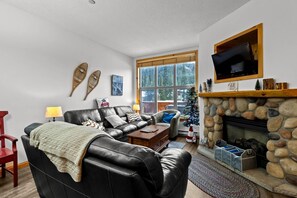 A cozy living room with a fireplace, a leather sofa, a coffee table, and a Christmas tree. - Crystal Forest #48 3 Bedroom Condo (Sun Peaks)