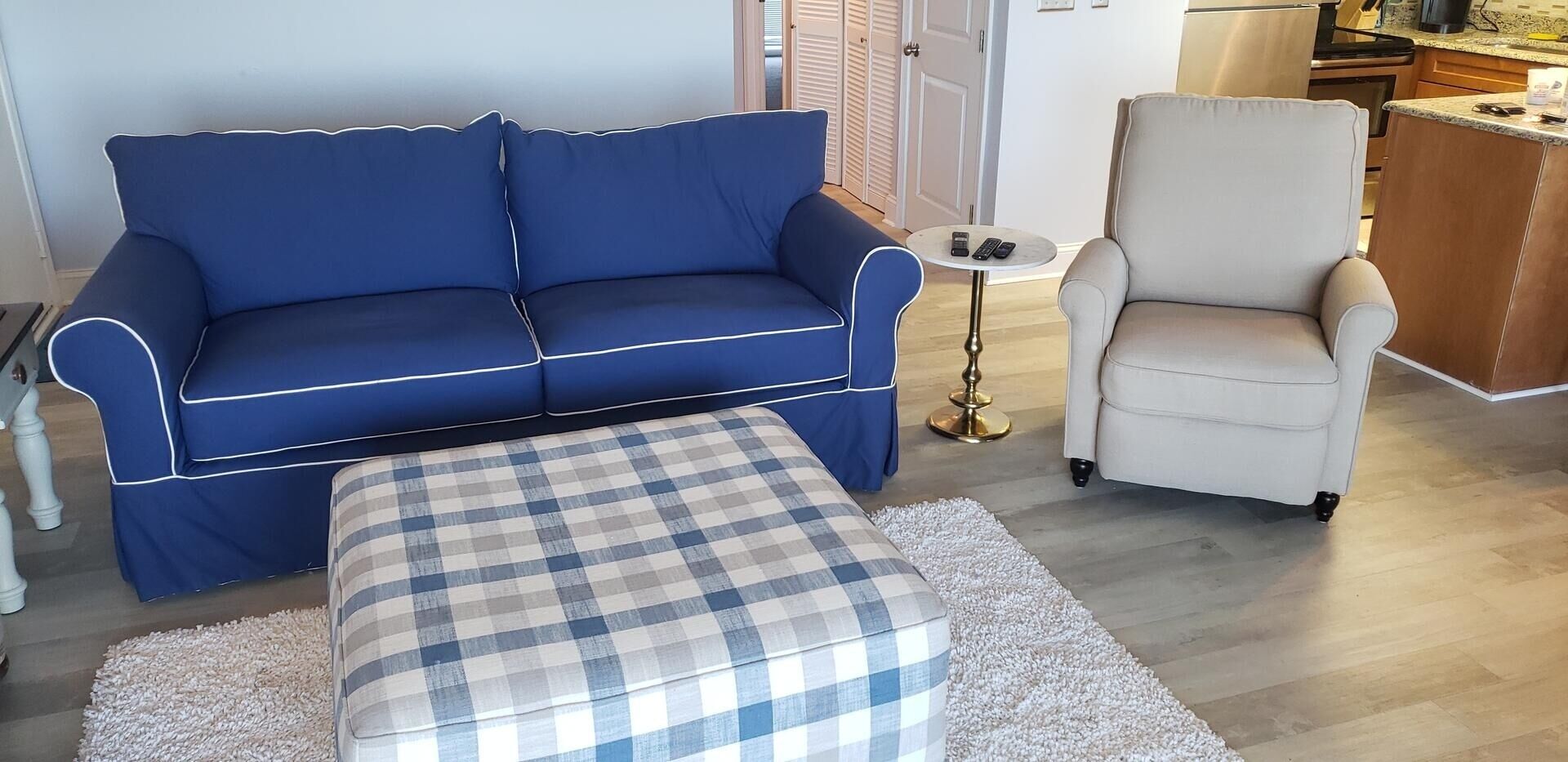 En stue med en blå sofa, en hvid lænestol og en ternet skammel.