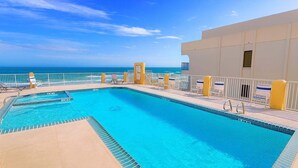 A rectangular pool with a clear blue water, surrounded by a white fence and yellow pillars, with a view of the ocean in the background. - Penthouse Beachfront Views Renovated 4 Bedroom Condo (South Padre Island)