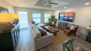A spacious living room with a large sofa, a coffee table, and a TV mounted on the wall. - Penthouse Beachfront Views Renovated 4 Bedroom Condo (South Padre Island)