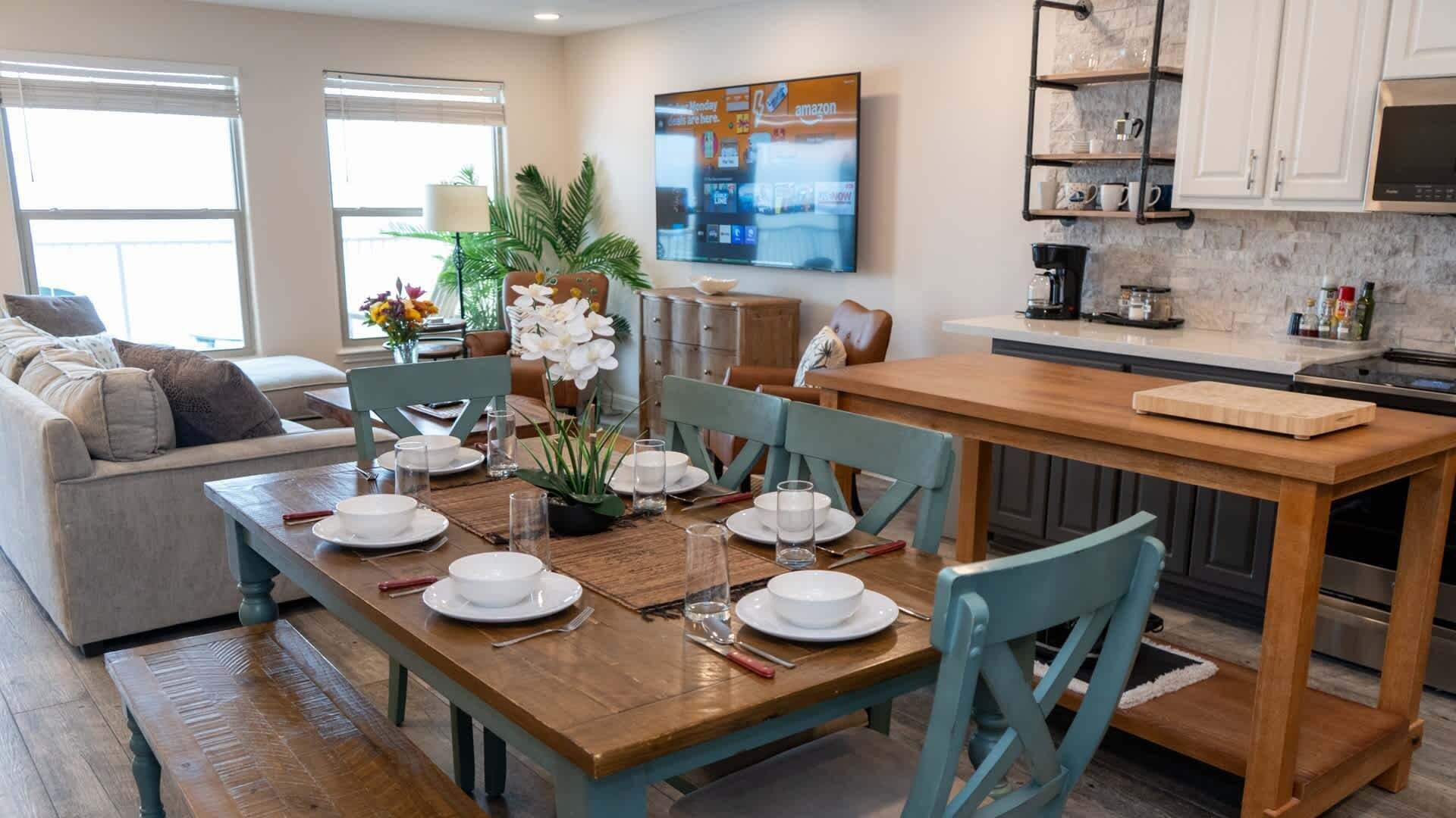 A modern kitchen with a wooden dining table set for four, a built-in oven, and a coffee station.
