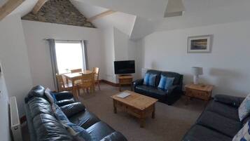 A living room with a stone ceiling, a black leather sofa, a wooden coffee table, a television, and a framed picture on the wall.
