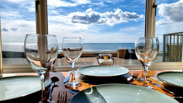 Taula preparada per dinar amb vista a la platja i l'oceà a través de grans finestres.