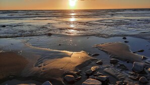 Una platja amb onades, roques i el sol ponent-se a l'horitzó.