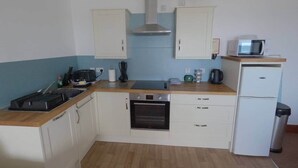 A compact kitchen with white cabinets, a built-in oven, a microwave, and a small refrigerator.