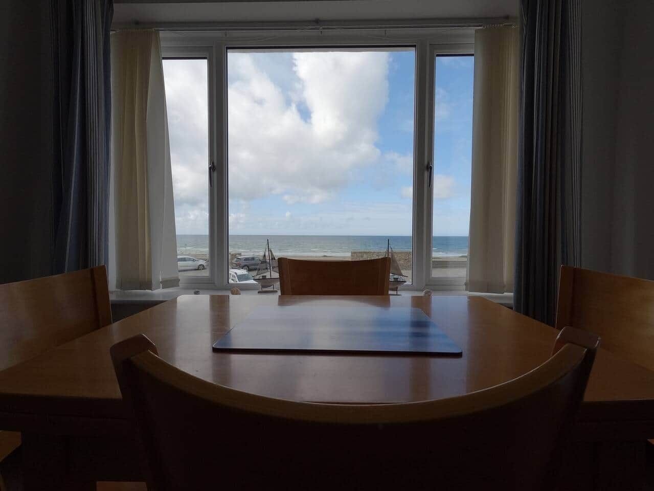 A room with a large window overlooking a beach, a round wooden table, and two chairs.