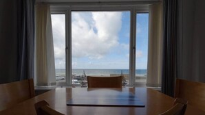 A room with a large window overlooking a beach, a round wooden table, and two chairs.