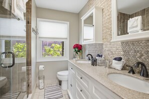Ein modernes Badezimmer mit zwei Waschbecken, Toilette, Dusche und einem großen Fenster.