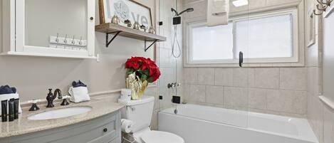 Un baño con lavamanos, tocador, inodoro y bañera. Cuenta con una ventana con vistas, ducha y un estante con artículos de aseo.