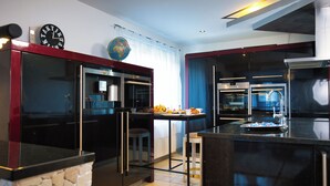 A modern kitchen with stainless steel appliances, a stone accent wall, and a dining area with a table set for two. - Modern Station Apartment Möhlin (Möhlin)