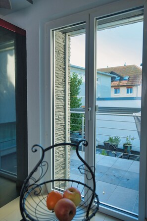 A room with a view through a glass door to a courtyard, a metal fruit basket on a windowsill, and a stone wall. - Modern Station Apartment Möhlin (Möhlin)
