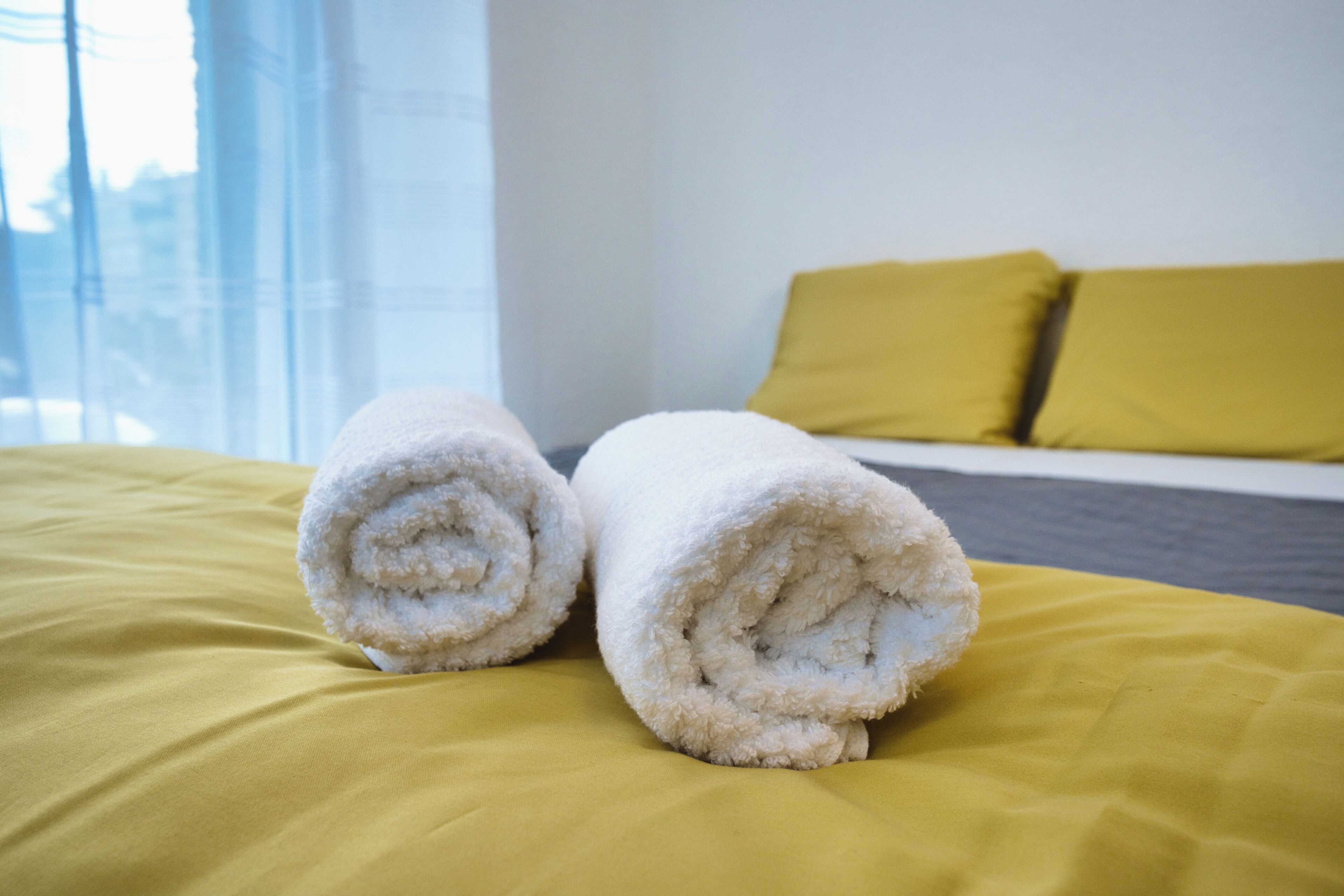 Ein Bett mit gelber Bettwäsche und zwei gerollten weißen Handtüchern.
