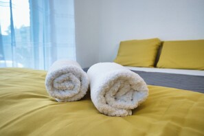 A bed with yellow bedding and two rolled white towels. - Modern Station Apartment Möhlin (Möhlin)