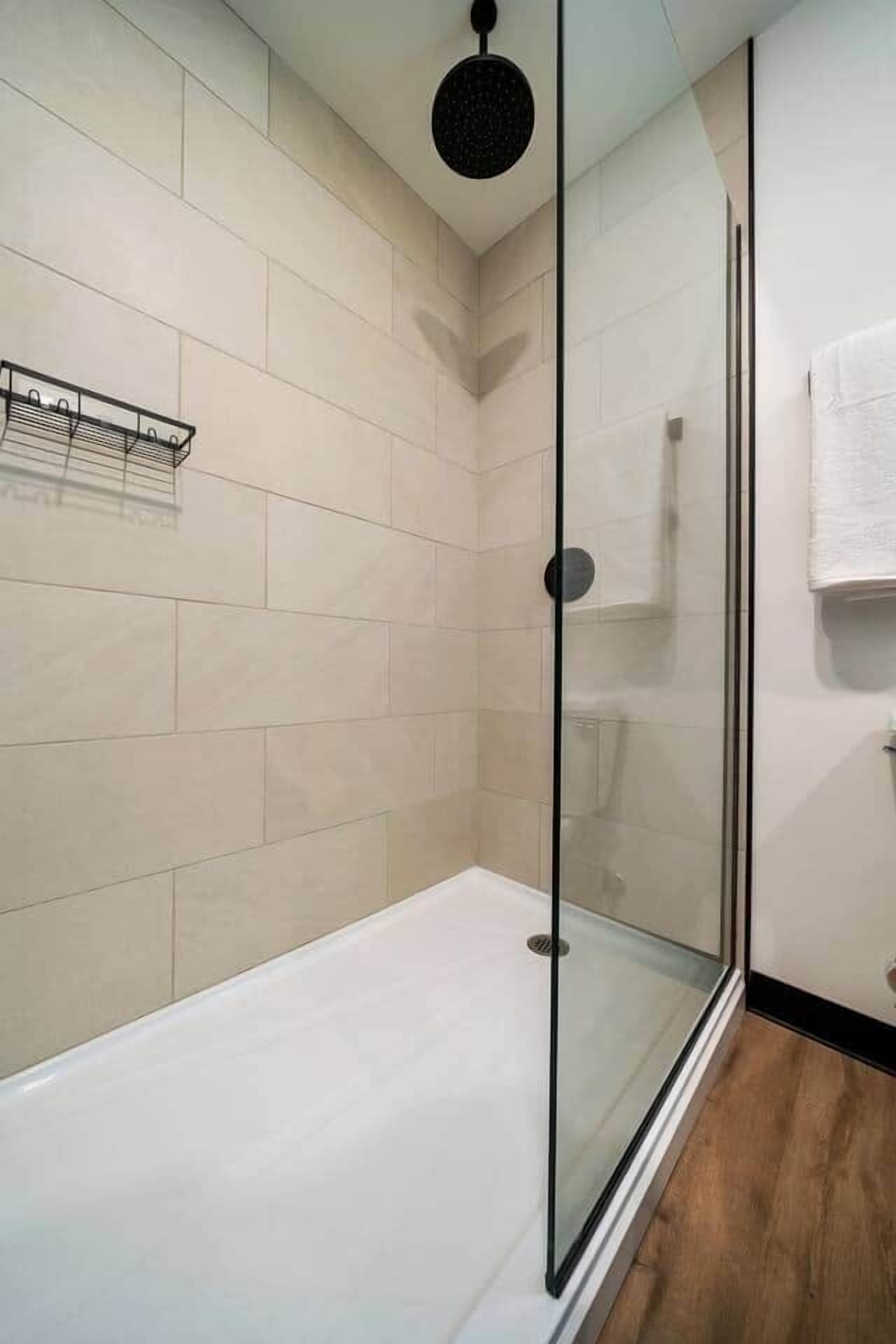Un baño moderno con cabina de ducha de vidrio, una bañera blanca y suelo de madera.
