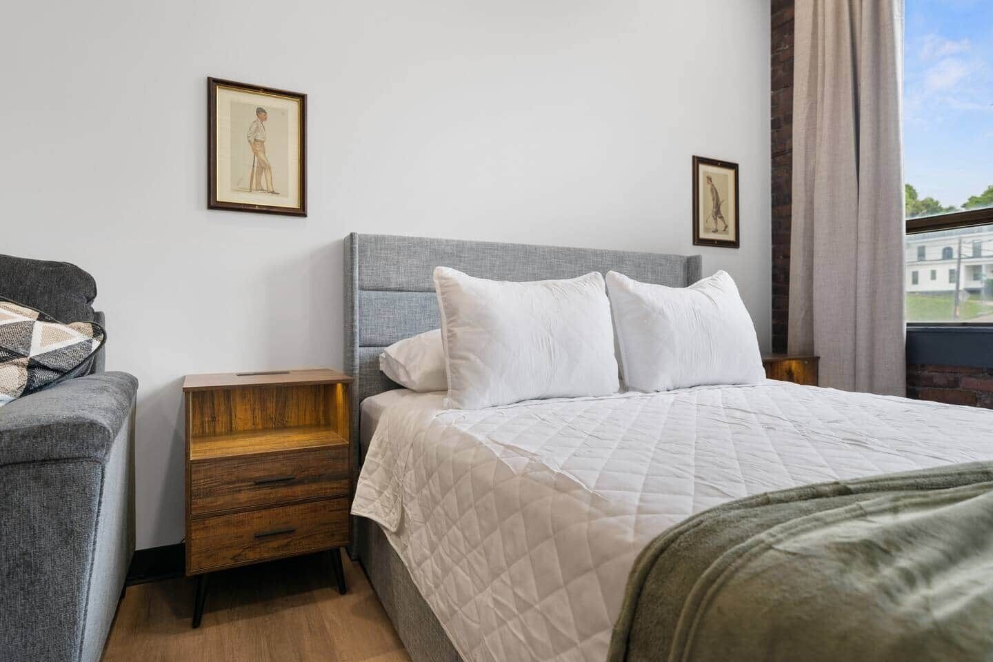 Une chambre d’hôtel avec un lit, une table de chevet, une chaise et deux tableaux encadrés au mur.