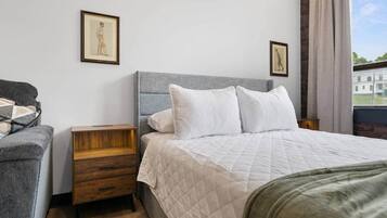 A hotel room with a bed, a nightstand, a chair, and two framed pictures on the wall.