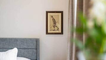 Un dormitorio con cama, mesita de noche, un cuadro enmarcado en la pared y una cortina que cubre parcialmente una ventana.