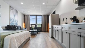A modern hotel room with a bed, a dining area, and a kitchenette.