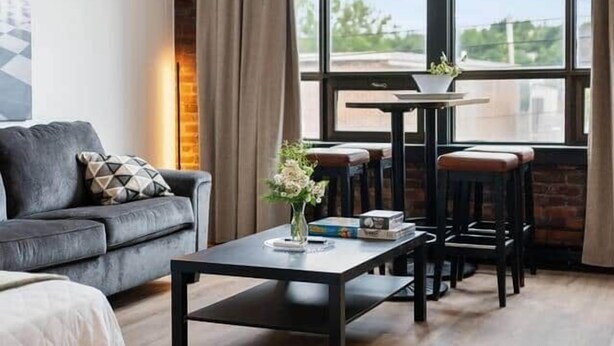 A modern hotel room with a large window, a sofa, a coffee table, and a small table with chairs.