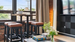 A modern bar area with stools, a table with a plant, and a TV mounted on a black acoustic panel wall.
