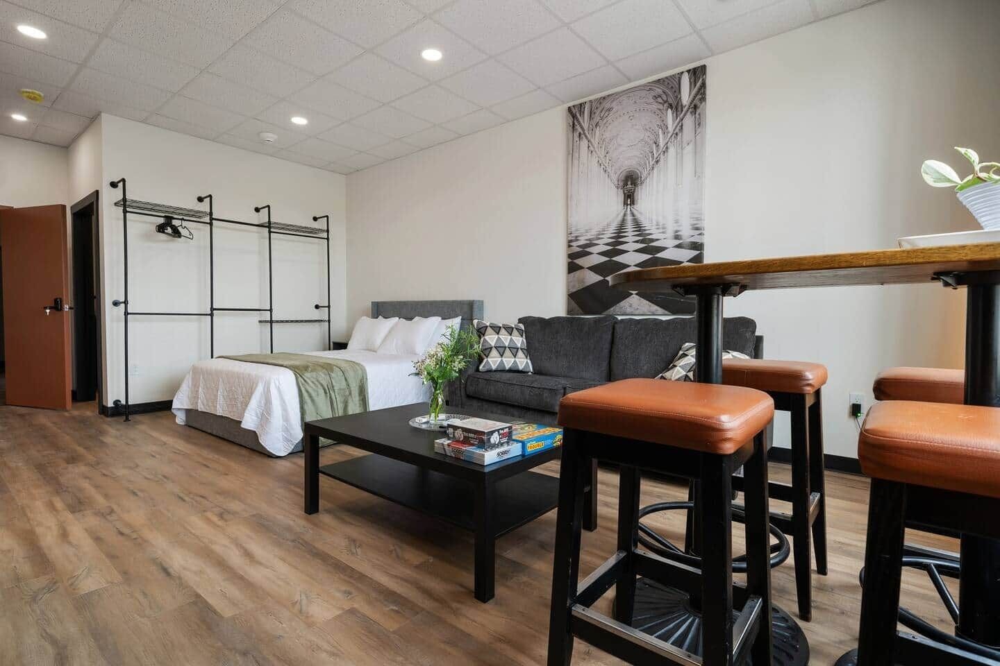 Una habitación de hotel moderna con una cama, un sofá, una mesita de centro y una zona de bar con taburetes.