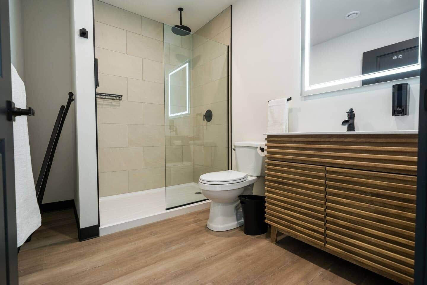 Ein modernes Badezimmer mit einer begehbaren Glasdusche, einer weißen Toilette und einem Holzwaschtisch.